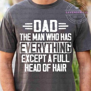 May include: Dark gray t-shirt with white text that reads "DAD THE MAN WHO HAS EVERYTHING EXCEPT A FULL HEAD OF HAIR." The shirt also has the text "Lavender Co" and "Since 2022" in a circular design.