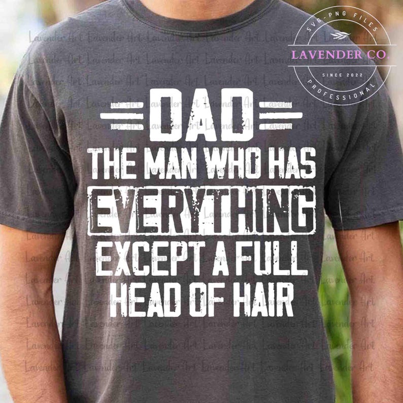 May include: Dark gray t-shirt with white text that reads "DAD THE MAN WHO HAS EVERYTHING EXCEPT A FULL HEAD OF HAIR." The shirt also has the text "Lavender Co" and "Since 2022" in a circular design.