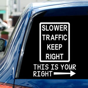 May include: A white vinyl decal applied to a car window. The decal features a rectangular sign with the words "SLOWER TRAFFIC KEEP RIGHT" in bold, black text. Below, the text "THIS IS YOUR RIGHT" is accompanied by a white arrow pointing right.
