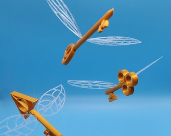 May include: Three gold-colored key-shaped ornaments with translucent wings. The wings are made of a delicate, intricate design. The keys are suspended in mid-air against a blue background.