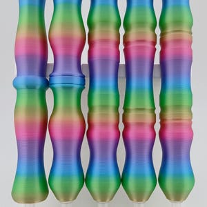 May include: Five rainbow-colored diamond painting pens are displayed vertically. Each pen has a unique shape and a gradient of colors, including pink, blue, green, and yellow. The pens are numbered 1 through 5 and are set in a white holder.