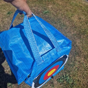 May include: A blue archery target bag with a white handle and a black and white archery target with red, yellow, and blue rings.