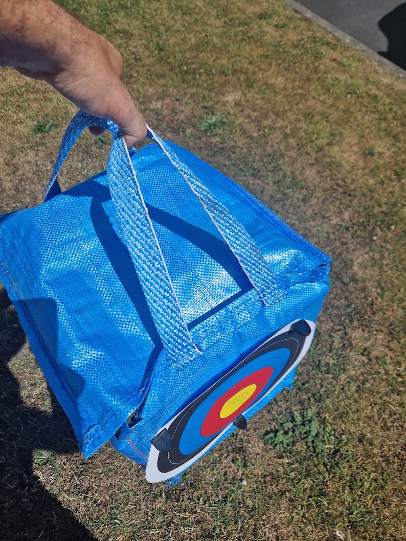 May include: A blue archery target bag with a white handle and a black and white archery target with red, yellow, and blue rings.