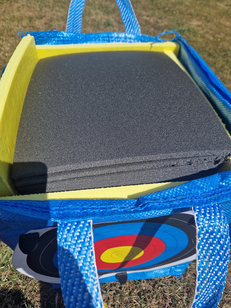 May include: A blue and yellow archery target bag with a black foam target inside. The bag has two handles and a zipper closure.