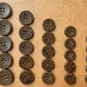 May include: Assortment of brown wooden buttons with different sizes and hole configurations. The buttons have a natural wood grain pattern.
