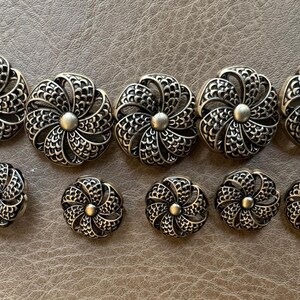 May include: A collection of antique silver-toned metal buttons. The buttons feature a floral design with a central raised bead and intricate openwork petals. The set includes both large and small sizes, suitable for various sewing projects.