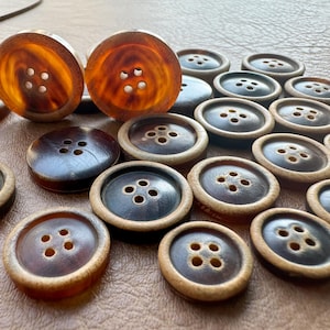 May include: A collection of brown buttons with four holes each. The buttons have a light brown rim and a darker brown center. Some buttons are standing upright, while others are lying flat.