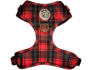 May include: Red and black plaid dog harness with a gold-colored metal ring for leash attachment. The harness features a round patch with the text "Hendricks and Maple". The harness is designed to fit around the dog's chest and shoulders.