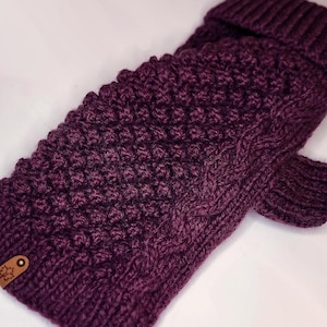 Peut inclure: Une paire de mitaines tricotées, de couleur violet foncé. Les mitaines présentent un motif texturé en relief et un poignet côtelé. Une petite étiquette en cuir marron avec un motif de flocon de neige est attachée.