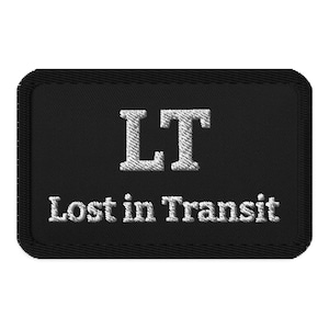 May include: Black rectangular patch with the embroidered text "LT" above "Lost in Transit" in white. The patch has a stitched border.