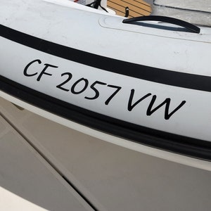 May include: Close-up of a white inflatable boat with a black stripe and the text "CF 2057 VW" written on it.