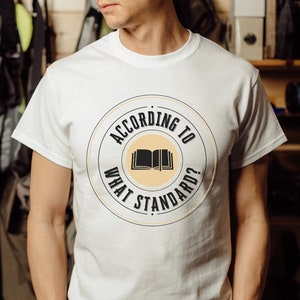 May include: White t-shirt with a circular graphic that says "According to What Standard?" with an open book icon inside the circle.