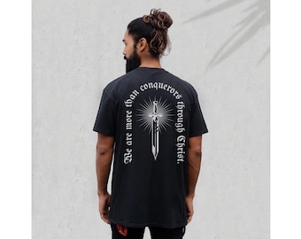 May include: Black t-shirt with a white graphic of a sword and the text "We are more than conquerors through Christ."