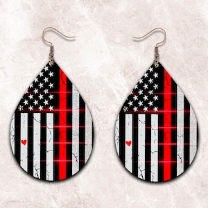 May include: A pair of teardrop-shaped earrings with a red, white, and blue American flag design. The flag has a thin red stripe down the center and a small red heart in the lower left corner.