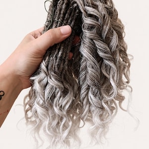 May include: A bundle of gray and white curly synthetic dreadlocks. The dreadlocks are a mix of dark gray and light gray, with a curly texture. The ends of the dreadlocks are a lighter shade of gray, creating a gradient effect. The dreadlocks are tied together with a green wire.