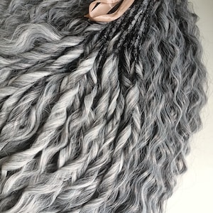 May include: A bundle of gray and white wavy hair extensions. The hair is braided and tied together with a ribbon.