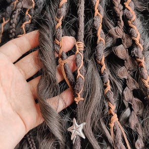 May include: Close-up of brown and black dreadlocks with leather wraps and a silver star charm.