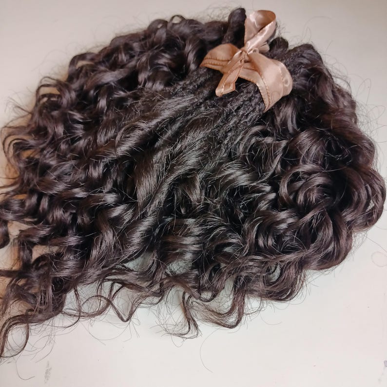 May include: Dark brown curly hair extensions tied with a light brown satin ribbon. The hair is tightly curled and appears to be a natural color. The hair extensions are bundled together.