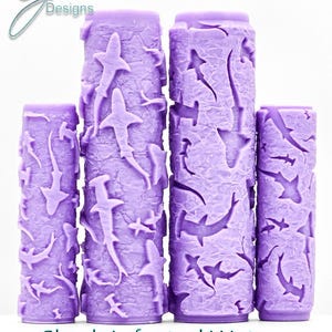 May include: Four cylindrical purple rollers featuring a raised, embossed pattern of various shark species and hammerhead sharks swimming amidst a textured, wavy water design. The text "G Designs" appears in the top left, with "Shark Infested Waters Intricate Texture" printed at the bottom.