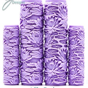 Puede incluir: Cuatro rodillos de pintura cilíndricos de color morado con un patrón en relieve de nenúfares y hojas de loto. Los rodillos están dispuestos en fila con el texto G Designs, Lilly Pads e Intricate Texture visible en la imagen.