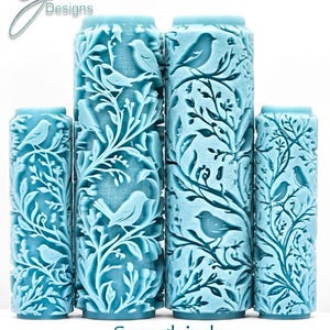 May include: A collection of four light blue cylindrical rollers with a detailed relief design of songbirds and foliage. The text "Songbirds Deep Impression" is visible at the bottom. The rollers vary in height.