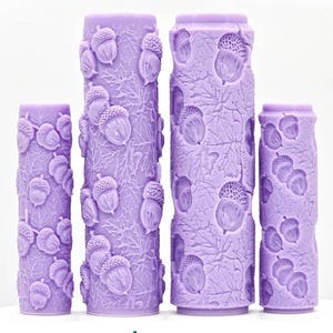 May include: Four lavender-colored cylindrical objects with an acorn and leaf pattern. The objects vary in height, with the tallest in the center. The text "Acorns Intricate Texture" is at the bottom.