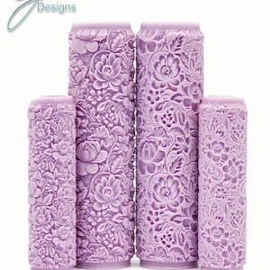 Puede incluir: Cuatro rodillos de amasar de color morado con intrincados diseños florales. Los rodillos de amasar están dispuestos en una pila vertical, con el más grande en la parte inferior y el más pequeño en la parte superior. El texto "DiaDeFlores Intricate Texture" está impreso debajo de los rodillos de amasar.