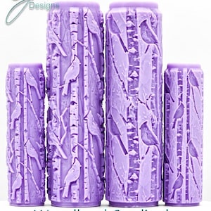Puede incluir: Cuatro rodillos cilíndricos de color lavanda con un patrón en relieve de cardenales posados en ramas de abedul. El texto G Designs aparece en la esquina superior izquierda y el texto Woodland Cardinals Intricate Texture está abajo.