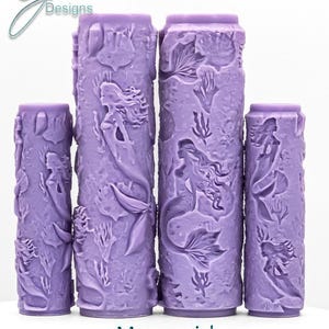 May include: Four lavender-colored cylindrical objects with mermaid and aquatic plant designs. The objects vary in height. The text "Mermaid Intricate Texture" is at the bottom. The top left corner has the text "G Designs".