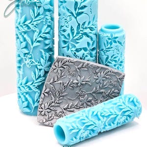 May include: A selection of blue texture rollers and a rectangular stamp, all featuring a detailed floral vine pattern. The rollers are of varying sizes. The text "Vines Deep Impression" is visible at the bottom of the image.
