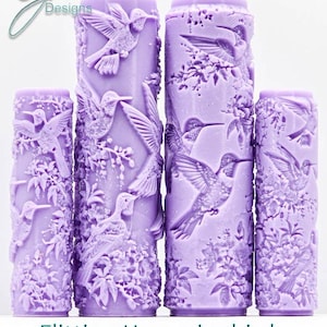 May include: Four lavender-colored cylindrical objects with detailed hummingbird and floral relief carvings. The objects vary in height. The text at the bottom reads "Flitting Hummingbirds Intricate Texture".