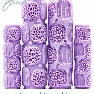 May include: Several lavender-coloured cylinders with carved pumpkin and floral patterns. The cylinders are of varying heights and feature detailed designs. The text "Carved Pumpkins Intricate Texture" is displayed below the cylinders.