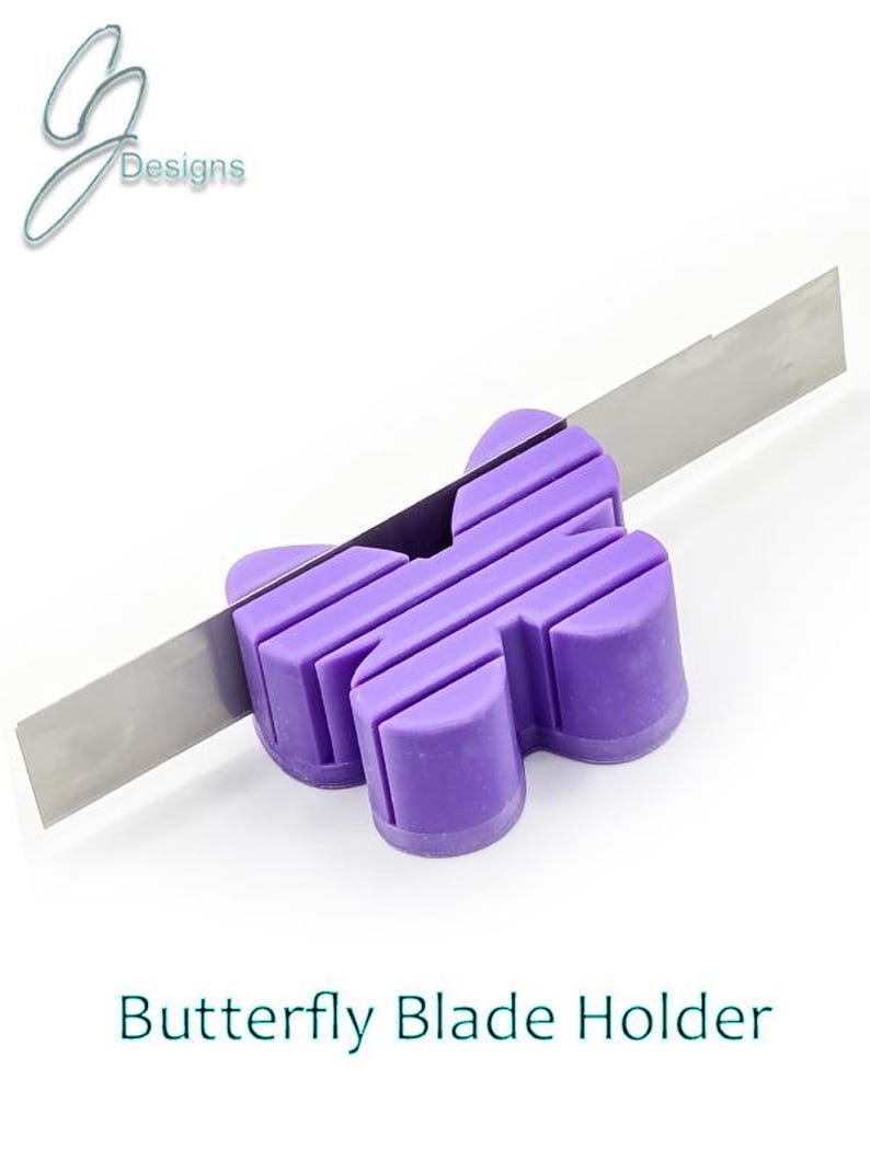 May include: Purple butterfly-shaped silicone blade holder with a silver blade resting on top.  The holder has a textured surface and is designed to hold a craft knife blade.