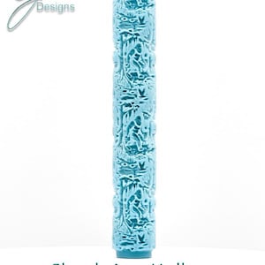 Puede incluir: Un rodillo de relieve cilíndrico de color azul claro con un patrón en relieve repetitivo de una criatura en un entorno forestal. El texto G Designs aparece en la esquina superior izquierda y Skunk Ape Hollow Double Tall Embossing debajo.