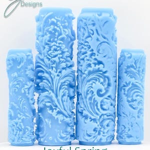 May include: Four light blue, cylindrical texture rollers with floral designs. The rollers vary in height and are arranged in a row. The text "Joyful Spring Deep Texture" is at the bottom. The logo "G Designs" is in the upper left corner.