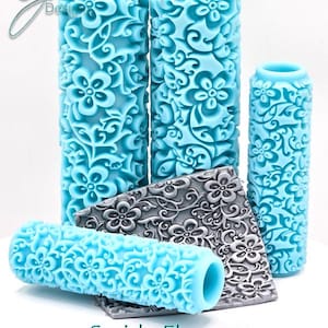 May include: A collection of turquoise floral pattern rolling pins and textured tiles. The rolling pins are cylindrical with a repeating flower and swirl design. The tiles are gray with a similar floral pattern. The text "Swirly Flowers Deep Impression" is at the bottom.