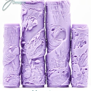 Peut inclure: Quatre cylindres lavande sculptés de lamantins et de scènes aquatiques. Les objets, de hauteurs variables, affichent le texte "Manatee Intricate Texture". Les cylindres ont une surface texturée et sont disposés verticalement.