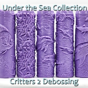 May include: Set of five purple rubber rollers with different under the sea designs. The designs include a fish, coral, dolphins, and whales. The text "Critters 2 Debossing" is printed below the rollers.