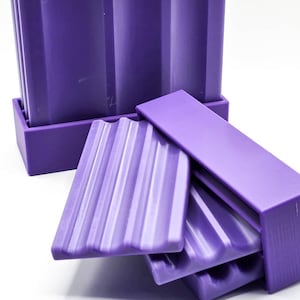 May include: A set of purple soap dishes with a ribbed design. The soap dishes are stacked in a rectangular holder, with some dishes partially removed. The background is white.