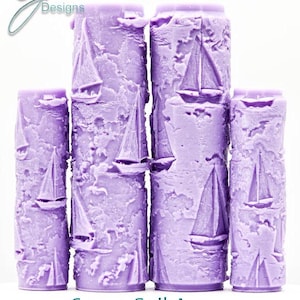 May include: Four lavender-colored, cylindrical candles with an intricate texture, each featuring a sailboat design. The candles are arranged in a row, with the text "Come Sail Away Intricate Texture" at the bottom. The "G Designs" logo is in the upper left corner.