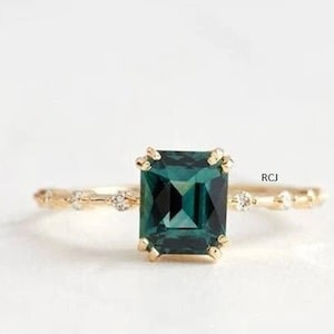 Puede incluir: Un anillo de oro con una piedra preciosa cuadrada verde esmeralda y pequeños diamantes engastados en la banda.