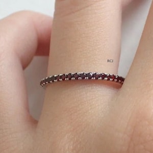Può includere: Un anello a fascia d'argento con una fila di piccole pietre preziose rosso scuro.