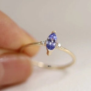 Puede incluir: Un anillo de oro con una piedra preciosa azul en forma de marquesa y dos pequeñas piedras blancas redondas en la banda.