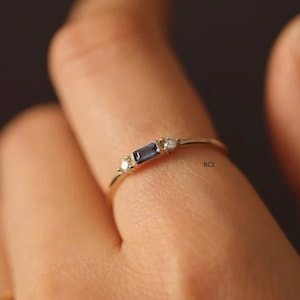 May include: A delicate gold ring featuring a small rectangular blue gemstone and two smaller round white gemstones.