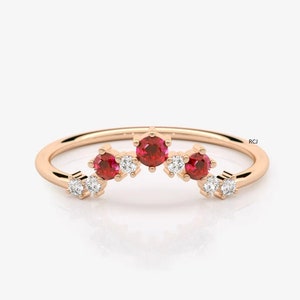 Op de afbeelding: Een delicate ring van roségoud met een gebogen rij rode robijnen en witte diamanten. De ring is geplaatst op een witte achtergrond.