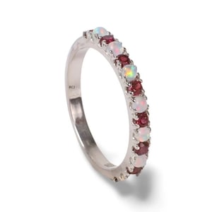 May include: A silver band ring with alternating white opal and red garnet gemstones. The ring is marked "RCJ" on the inside.