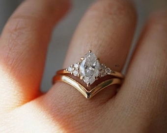 May include: A gold engagement ring with a pear-shaped diamond and smaller diamonds set in a delicate band. The ring is worn on a finger with a matching gold band.