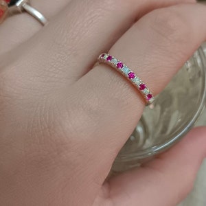 May include: A silver band ring with alternating pink and white stones. The ring is on a person's finger.