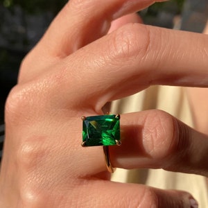 May include: A gold ring with a large, emerald green square-shaped gemstone.