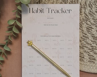 May include: A pink habit tracker with a gold pen and a bee-shaped topper. The tracker has a section for a new habit, why you want it, and a grid for 30 days. The text on the tracker says "Habit Tracker", "New Habit", "Why do you want this?", "Tick each day you make progress", and "Moon & Living".